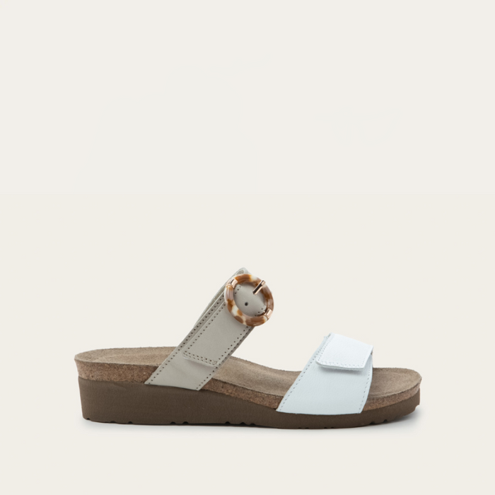 A pair of women's wide-width sandals in beige and white colors, featuring a hook and loop faux buckle accent and an open back design.