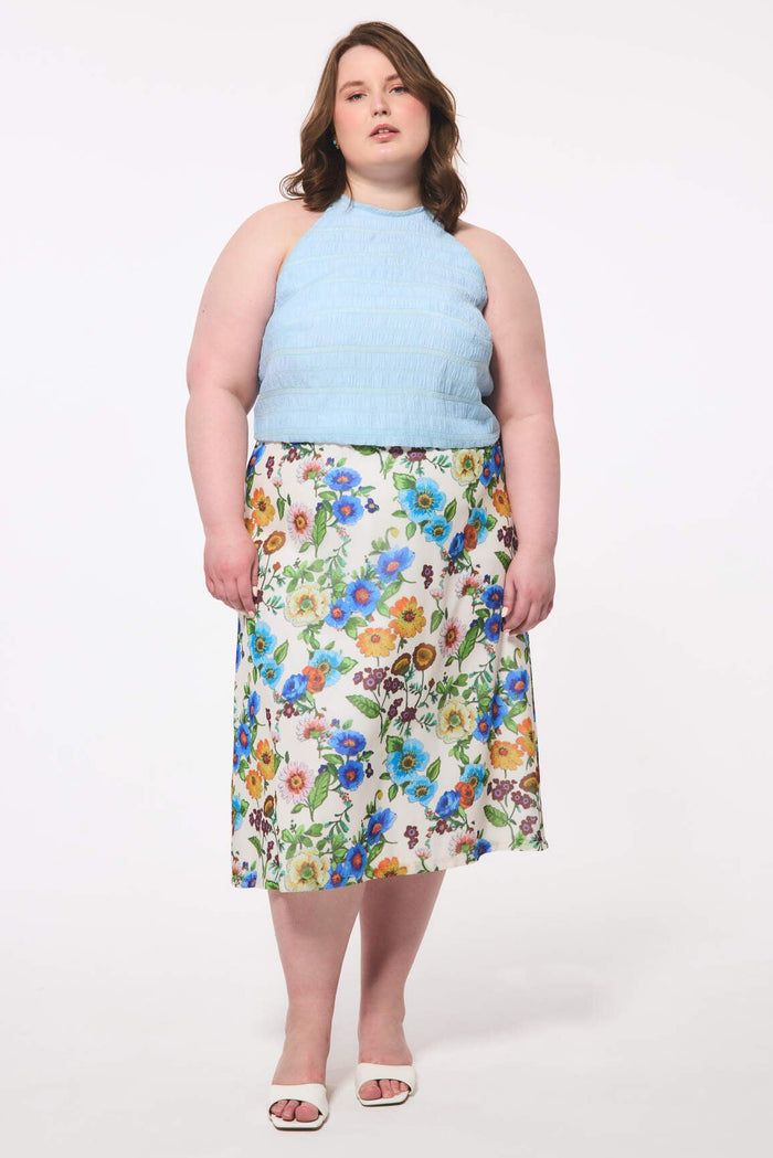Plus size woman wearing a light blue sleeveless top and floral skirt on a white background