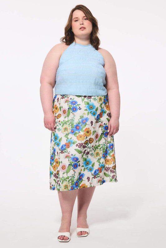 Plus size woman wearing a light blue sleeveless top and floral skirt on a white background