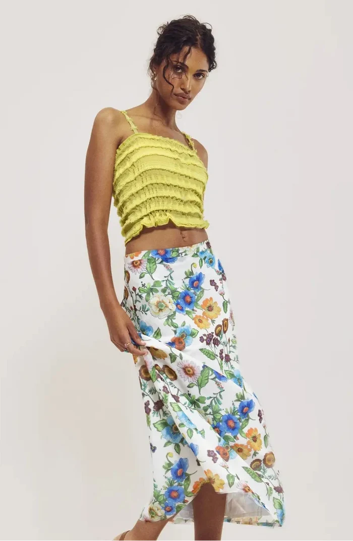 Woman wearing a yellow top and floral skirt on a plain background