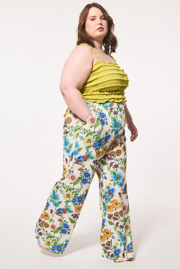 Plus size woman wearing a yellow top and floral pants on a white background