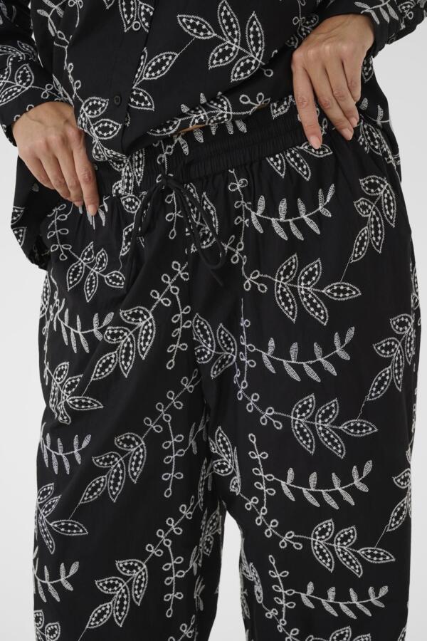 Black pants with white leaf pattern worn by a person on a neutral background