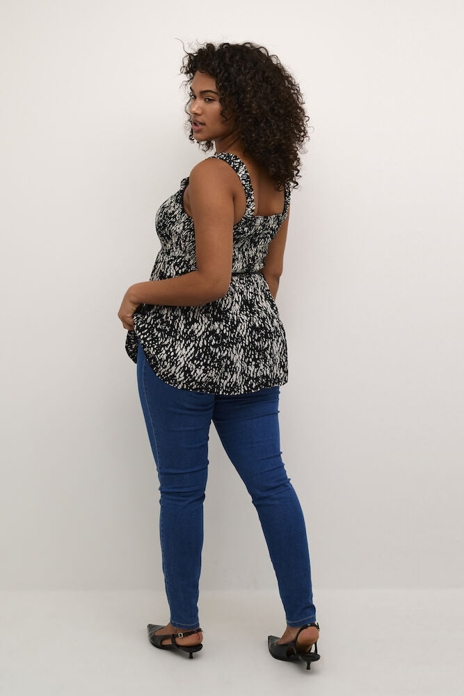 Woman wearing a black and white patterned top and blue jeans against a white background