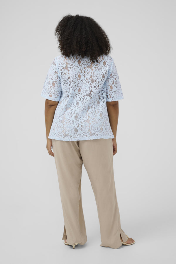 Person wearing a light blue lace top and beige pants on a white background