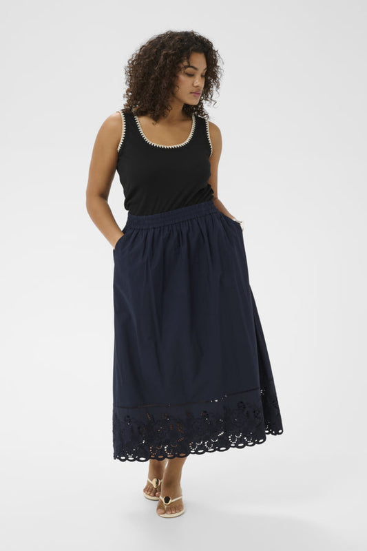 Woman wearing a black sleeveless top and navy skirt with lace trim on a white background
