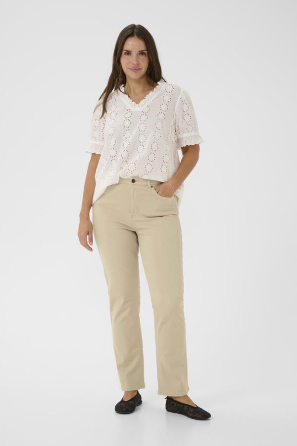 Woman wearing a white blouse with lace details and beige pants on a white background