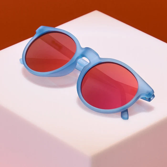 Product close up of circle-framed sunglasses, featuring light blue frames and red reflective lenses.