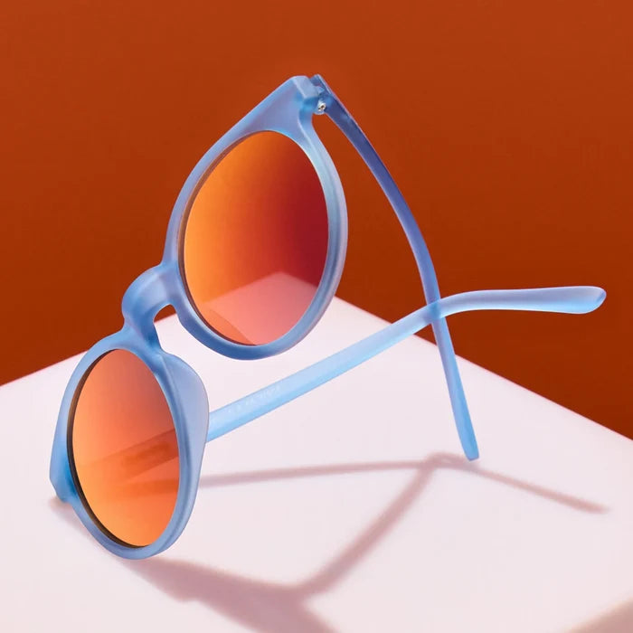 Product close up of circle-framed sunglasses, featuring light blue frames and red reflective lenses.