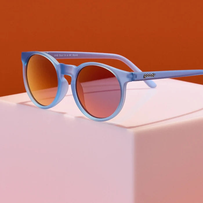 Product close up of circle-framed sunglasses, featuring light blue frames and red reflective lenses.