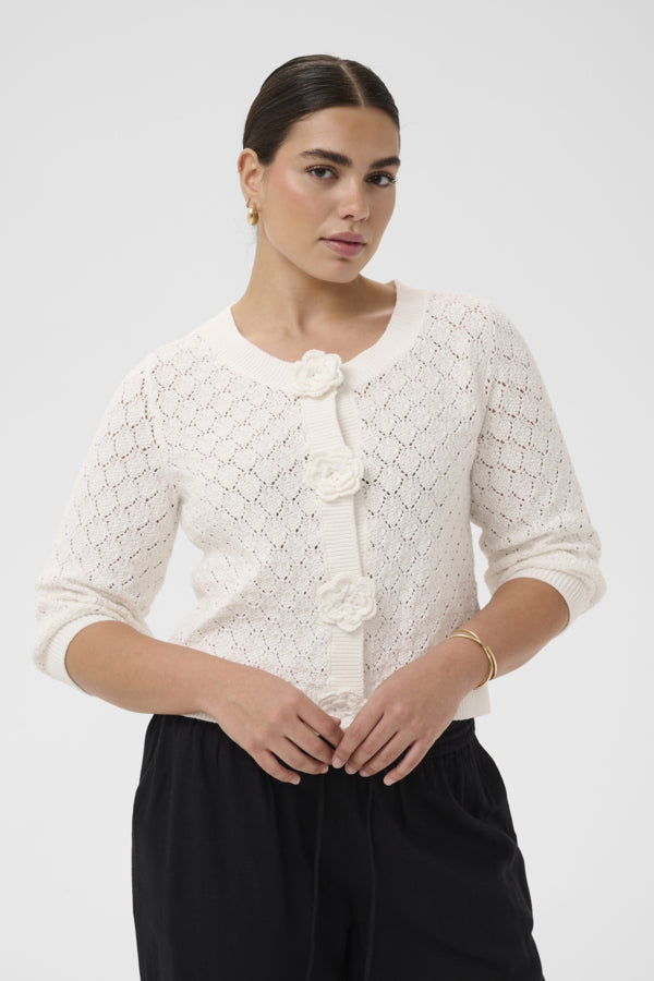 Woman wearing a white textured cardigan with floral buttons on a plain background