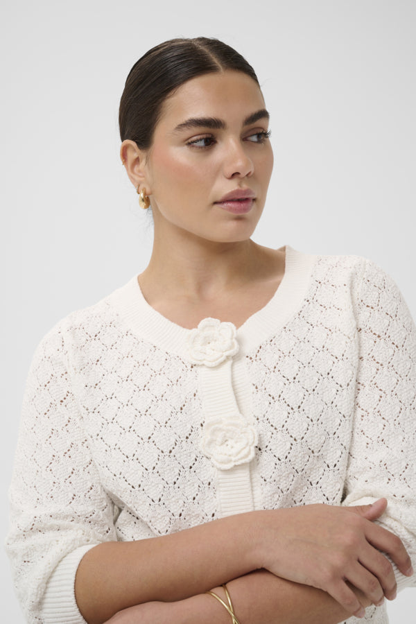 Woman wearing a white lace cardigan with a floral detail on a light gray background