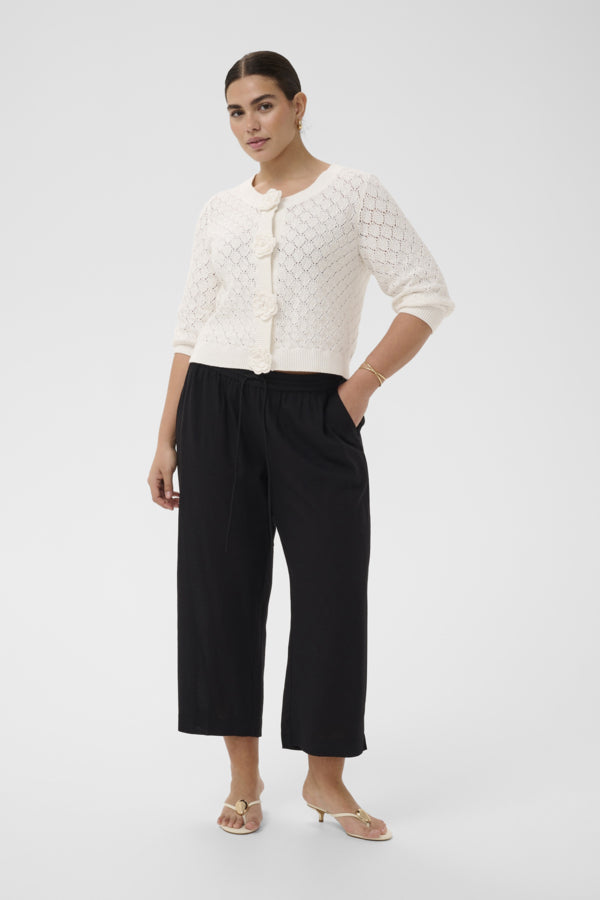 Woman wearing a white textured top and black pants on a white background