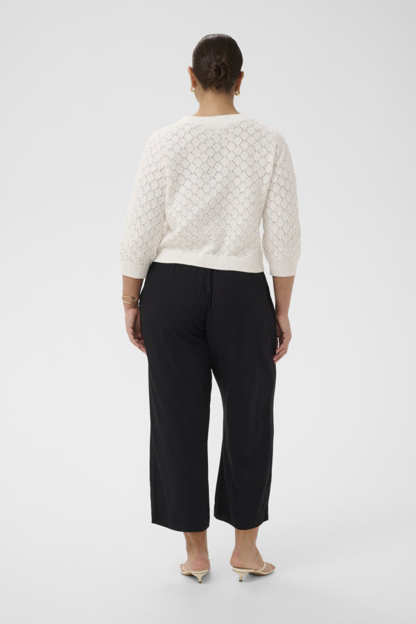 Person wearing a white textured sweater and black pants on a white background