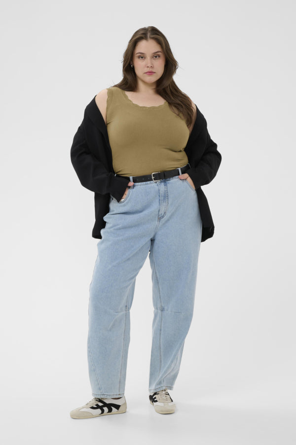 Woman wearing a green tank top, black jacket, light blue jeans, and black and white sneakers on a white background
