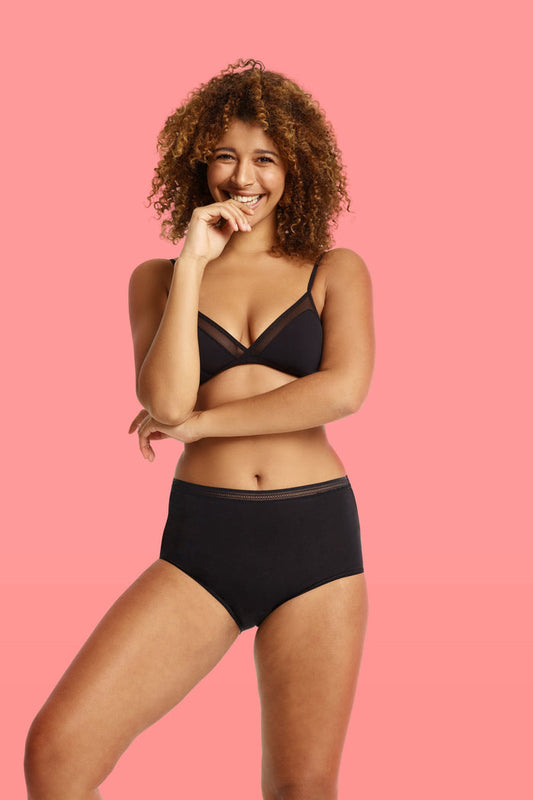 Woman wearing a black bra and love luna lady leaks full briefs set on a pink background