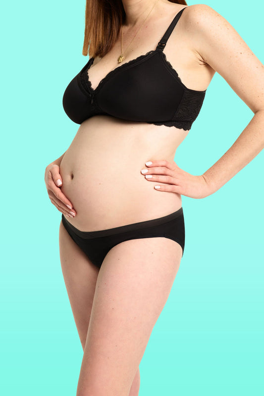 Pregnant woman wearing a black maternity bra and love luna lady leaks maternity bikin briefs  against a teal background