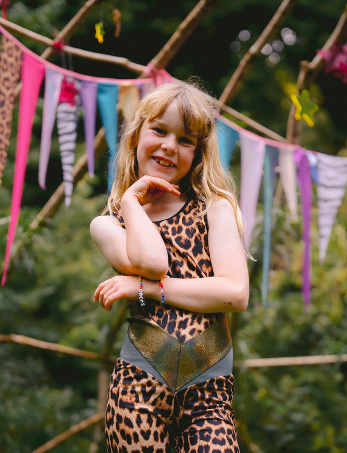 Young girl in a leopard print outfit standing in front of colorful flags.