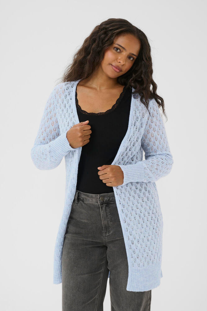 Woman wearing a light blue cardigan over a black top and gray pants on a white background