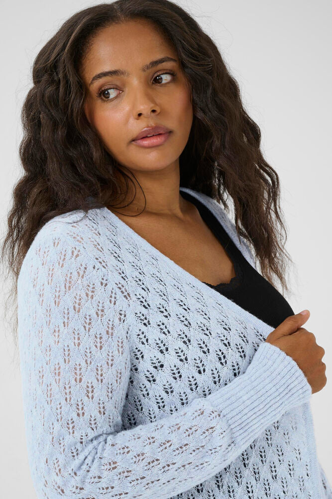 Woman wearing a light blue lace cardigan over a black top against a white background