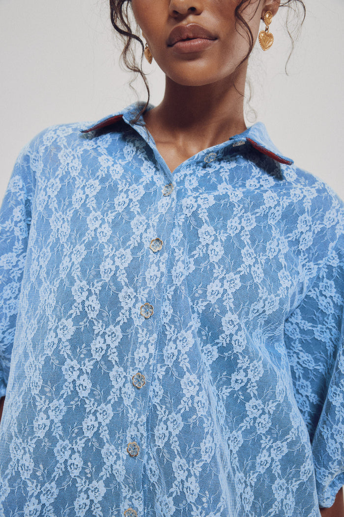 Person wearing a blue lace shirt with a plain background