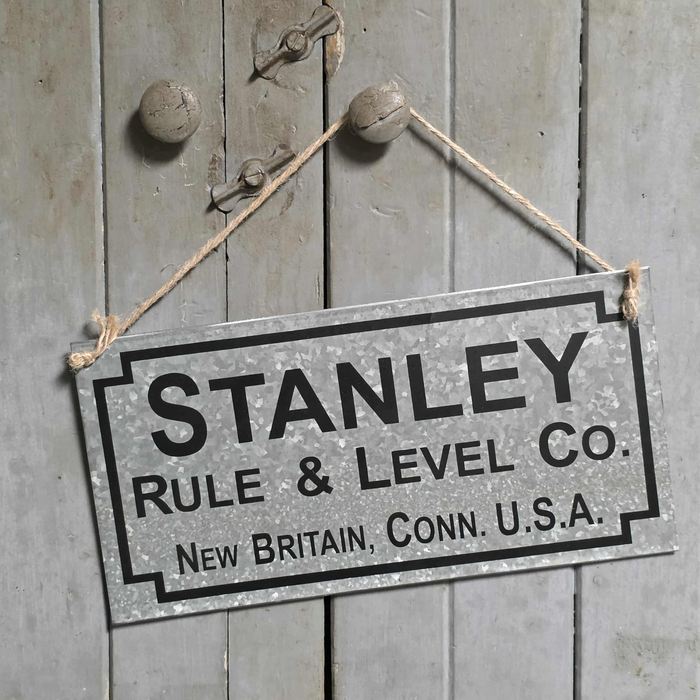 Vintage-style sign for Stanley Rule & Level Co. hanging on a wooden door.