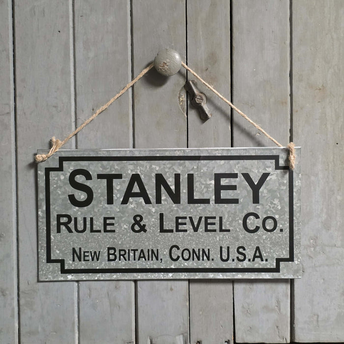 Vintage-style sign for Stanley Rule & Level Co. hanging on a wooden wall.