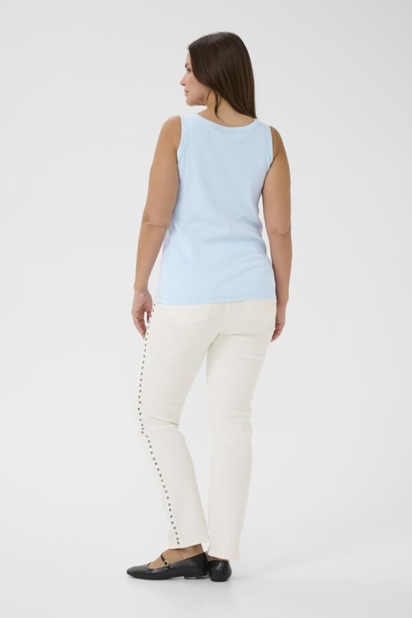 Woman wearing a light blue sleeveless top and white pants on a white background