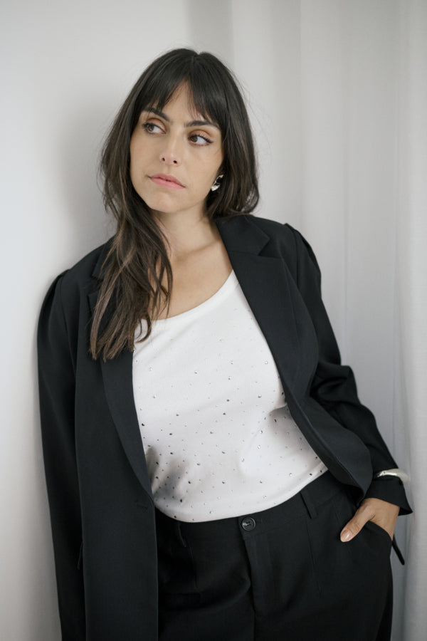 Woman wearing a black blazer over a white top with black polka dots against a plain background