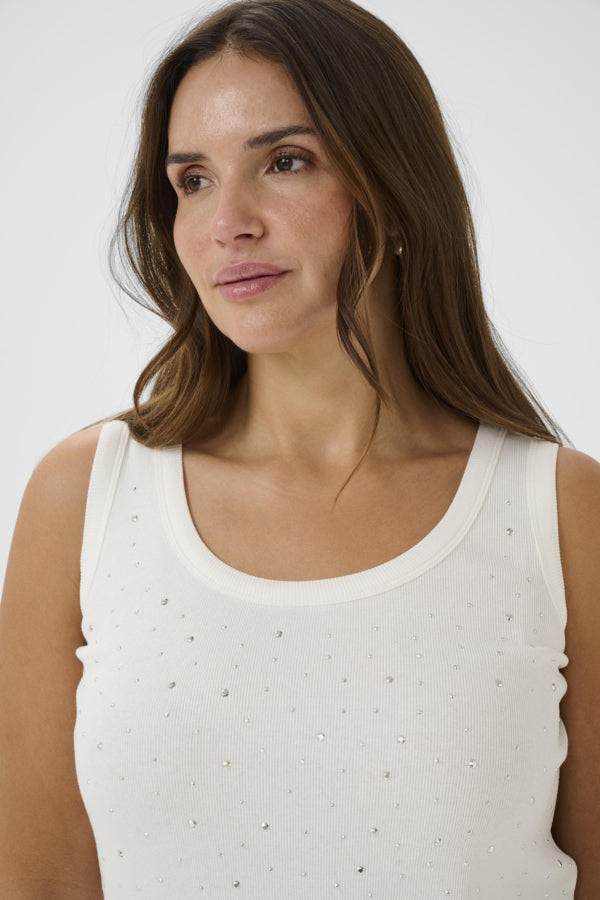 Woman wearing a white tank top with small embellishments against a plain background