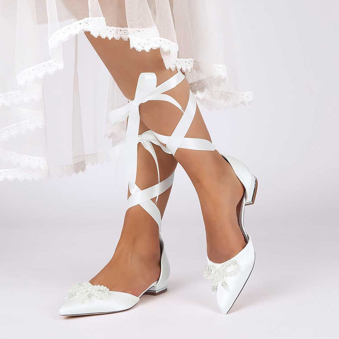 White bridal ankle strap flat shoes with lace ribbons and bow detail for elegant bridal outfits