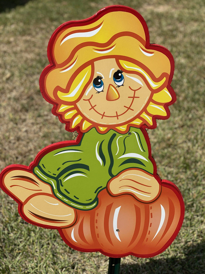 Fall and autumn outdoor yard decor signs with stakes featuring a cartoon scarecrow girl sitting atop of an orange pumpkin.  Perfect for autumn, Thanksgiving or Halloween outdoor decorating. All fall lawn signs come with stakes for easy placement, mounting and install. Place in your yard, garden, drive, walkway, even front porch, back deck or patio.